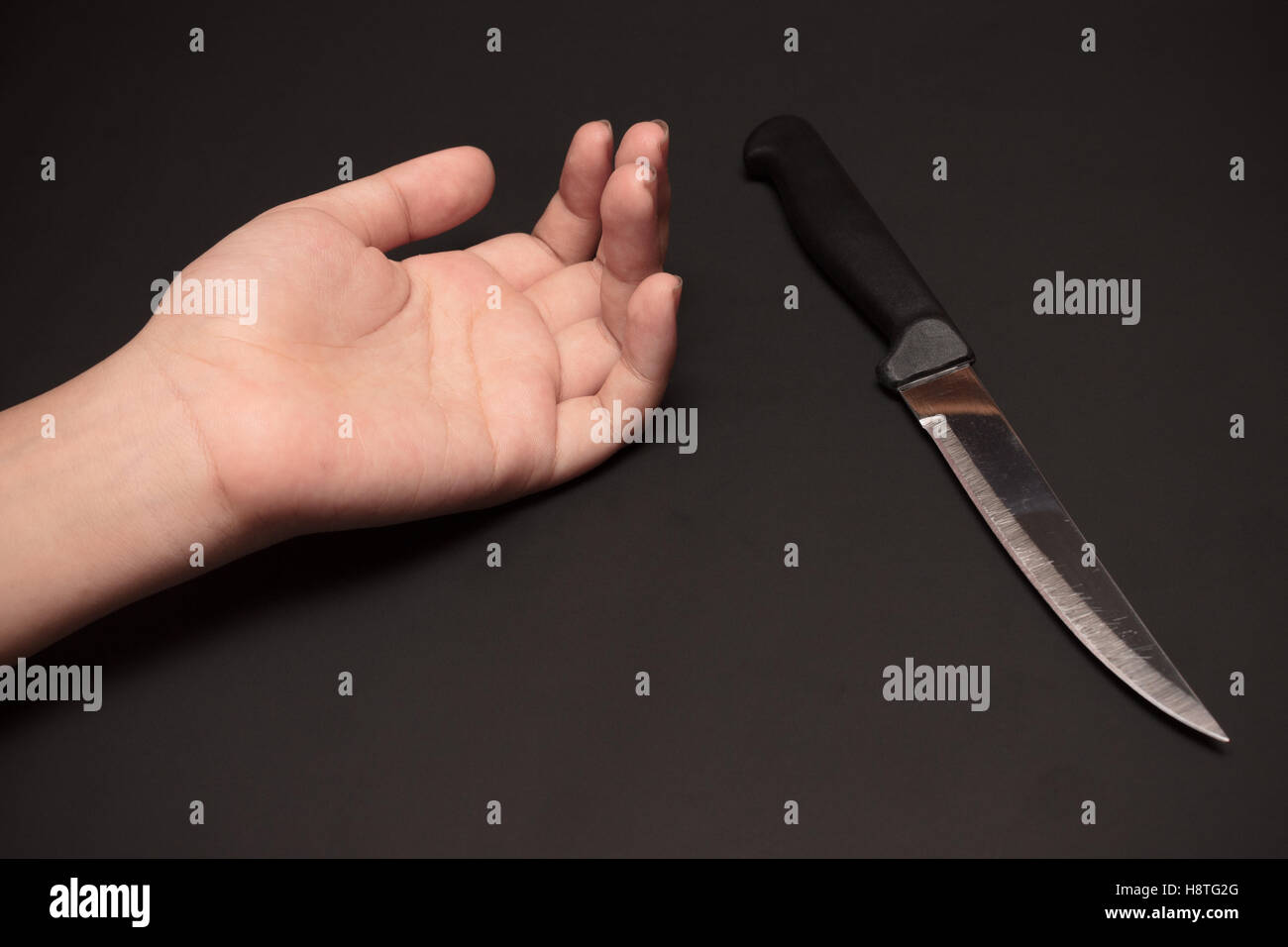 Un couteau de cuisine à côté de la main de quelqu'un sur fond sombre. Cette image a été tourné avec un seul flash bouncing technique. Banque D'Images