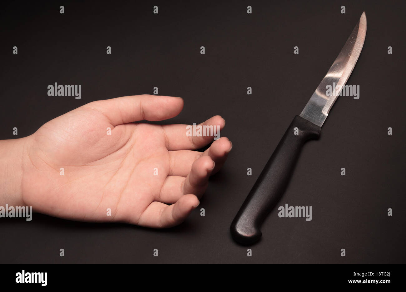 Un couteau de cuisine à côté de la main de quelqu'un sur fond sombre. Cette image a été tourné avec un seul flash bouncing technique. Banque D'Images