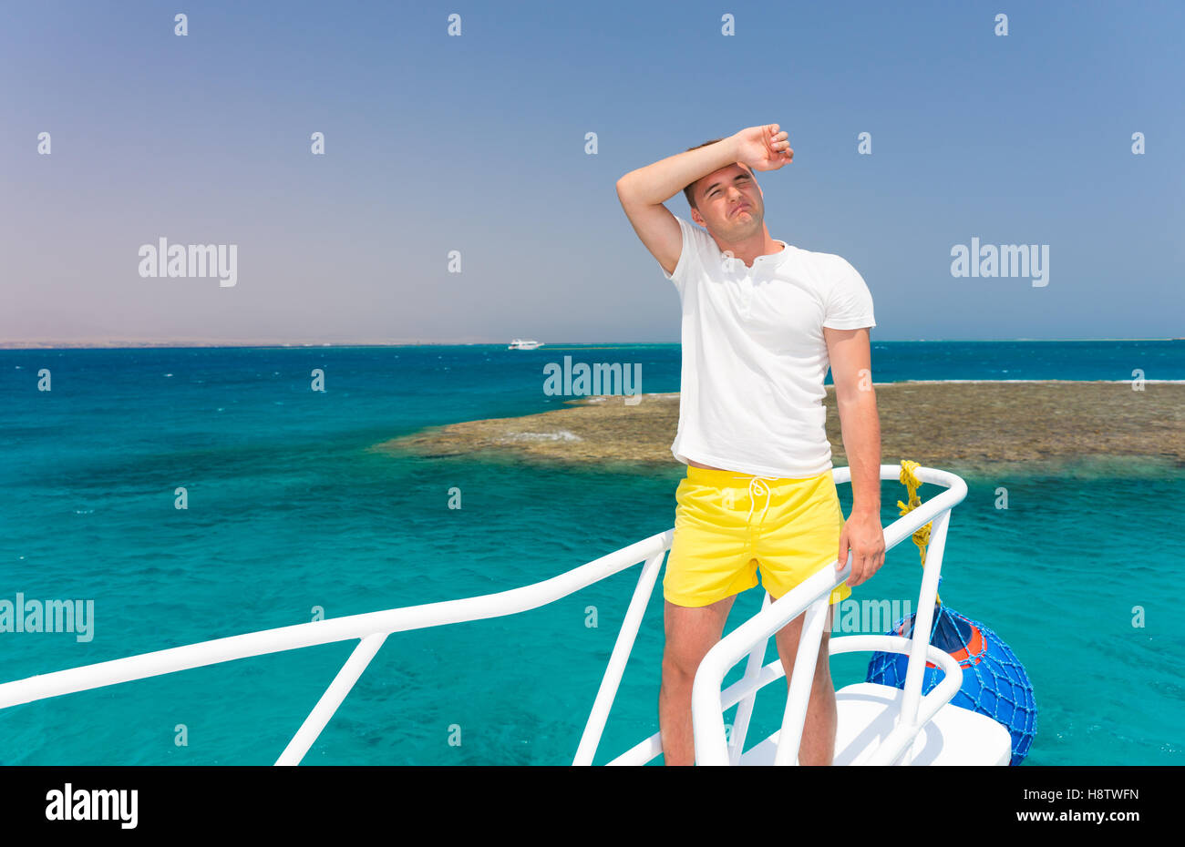 Bel homme fatigué debout sur le yacht lors d'une journée ensoleillée, belle mer turquoise sur fond de Banque D'Images