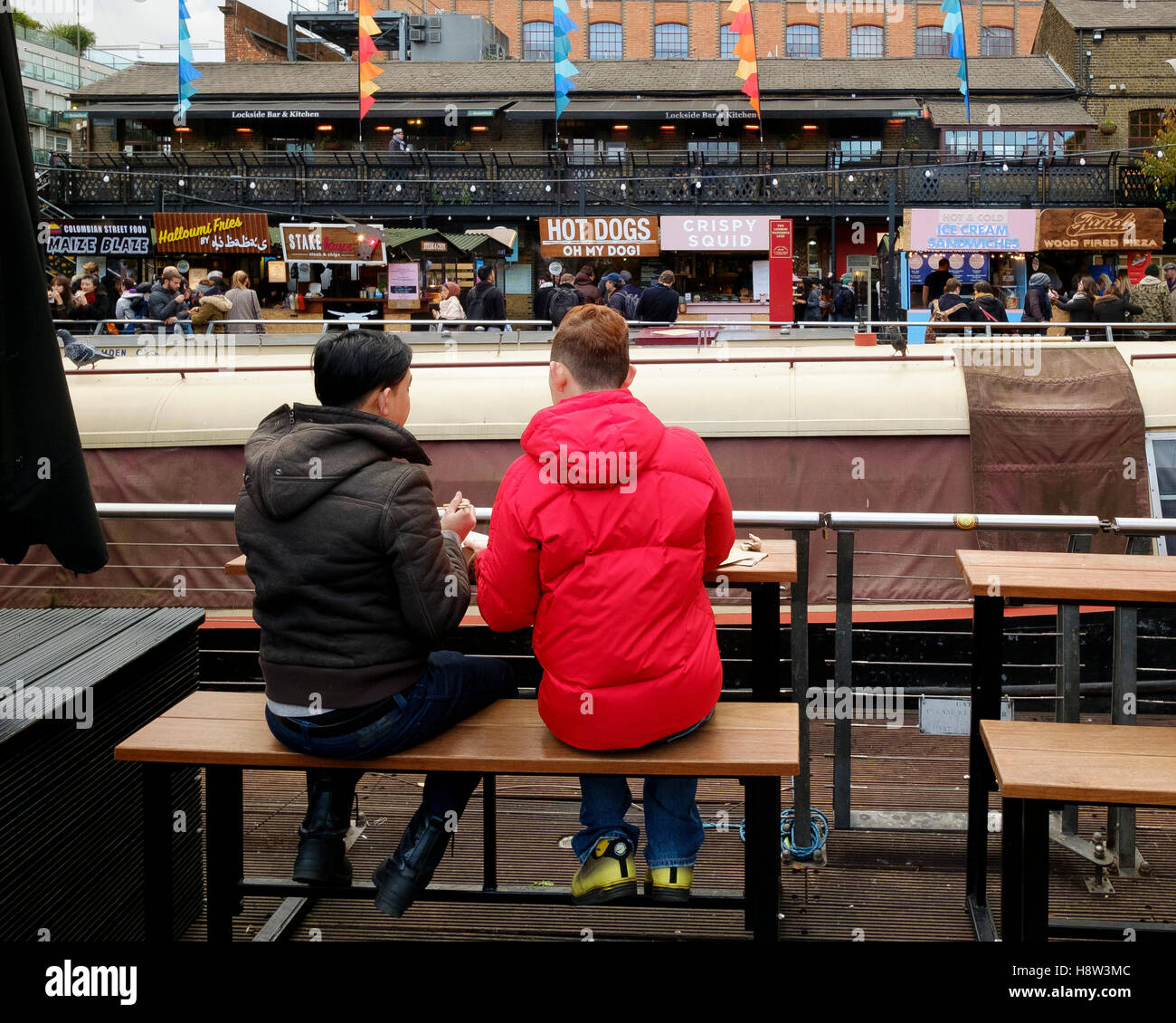 Deux touristes s'asseoir sur un banc en face de l'alimentation de rue cale au Camden Lock Market, Camden Town, London Banque D'Images
