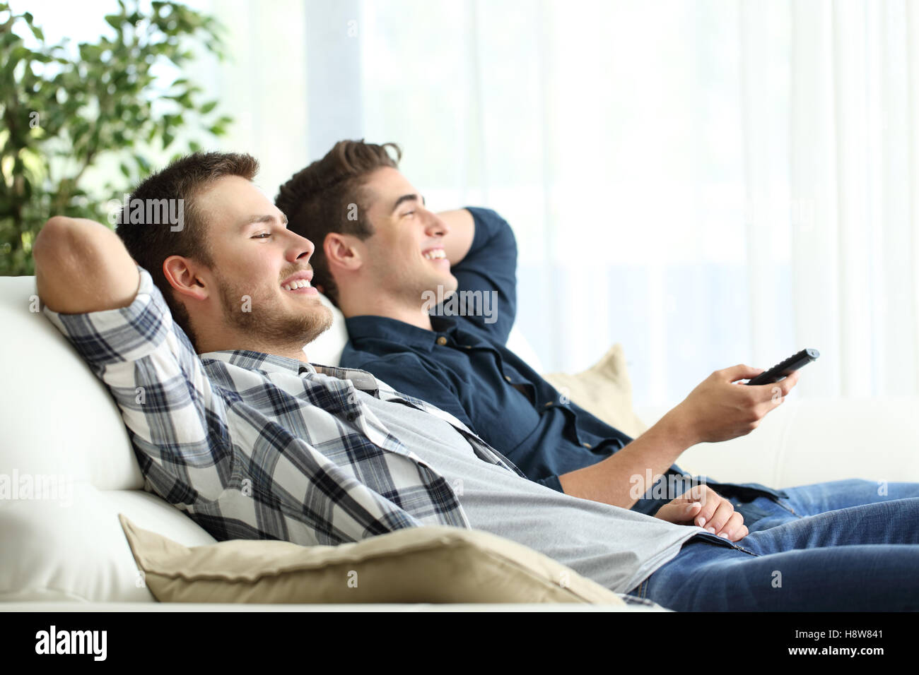 Vue de côté portrait de deux colocataires en regardant la télé assis dans un canapé confortable dans le salon à la maison Banque D'Images