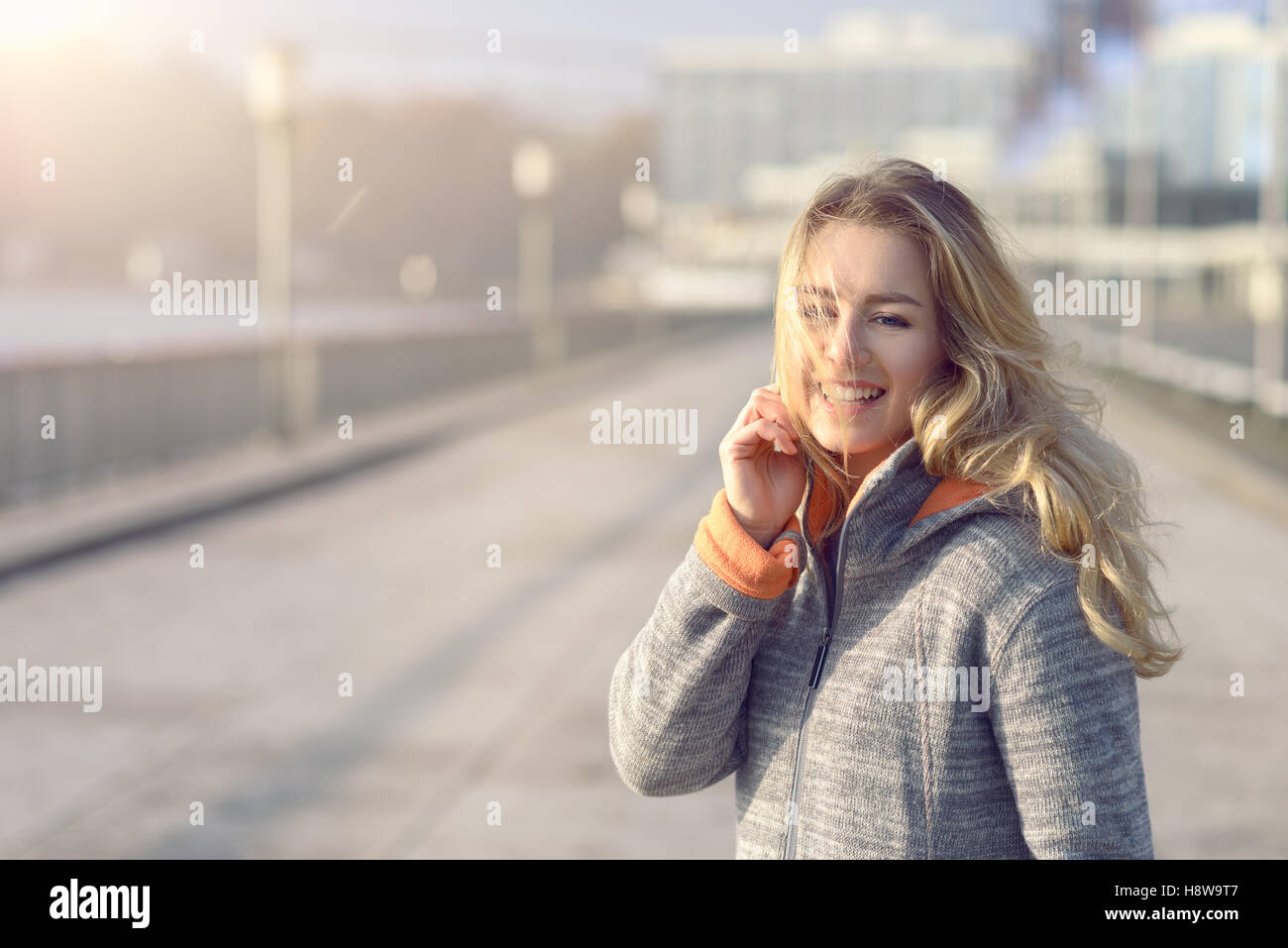 Femme heureuse avec un beau sourire debout dans son manteau sur un front de mer en hiver regardant la caméra avec une expression joyeuse Banque D'Images