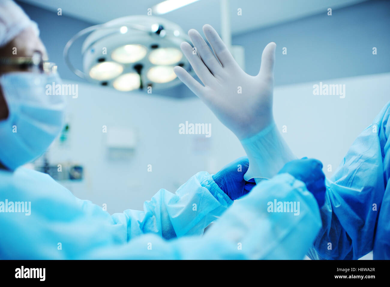Aide Assistant Le chirurgien mis sur des gants en latex avant l'opération. Une équipe de chirurgiens dans le fond de la lampe d'exploitation prepar Banque D'Images