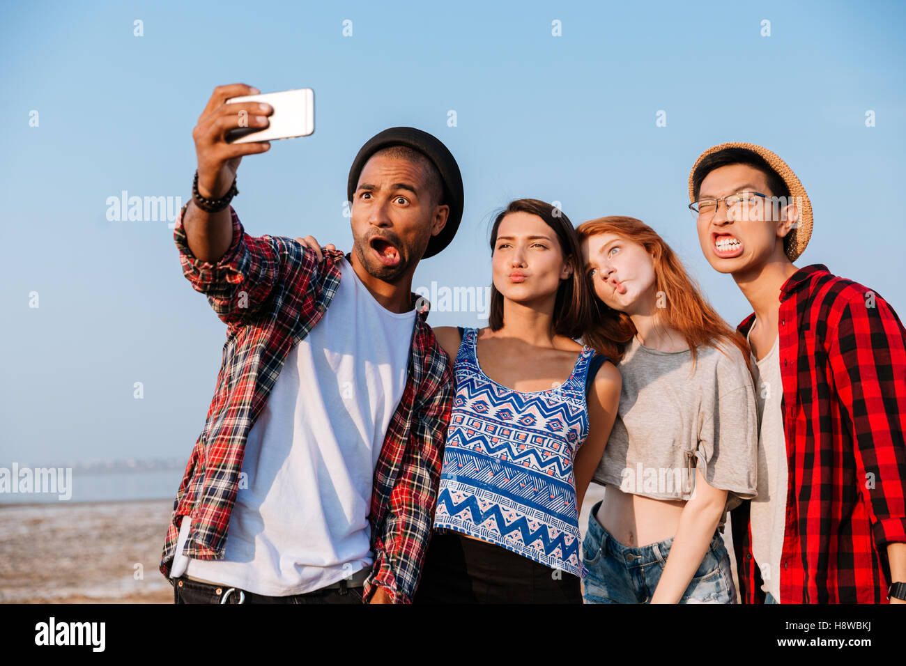 Groupe de jeunes amis amusant en tenant avec selfies téléphone cellulaire et faire des grimaces à l'extérieur Banque D'Images