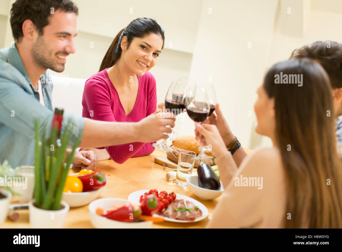 Groupe d'happ jeunes assis près de la table à manger et à boire du vin rouge Banque D'Images