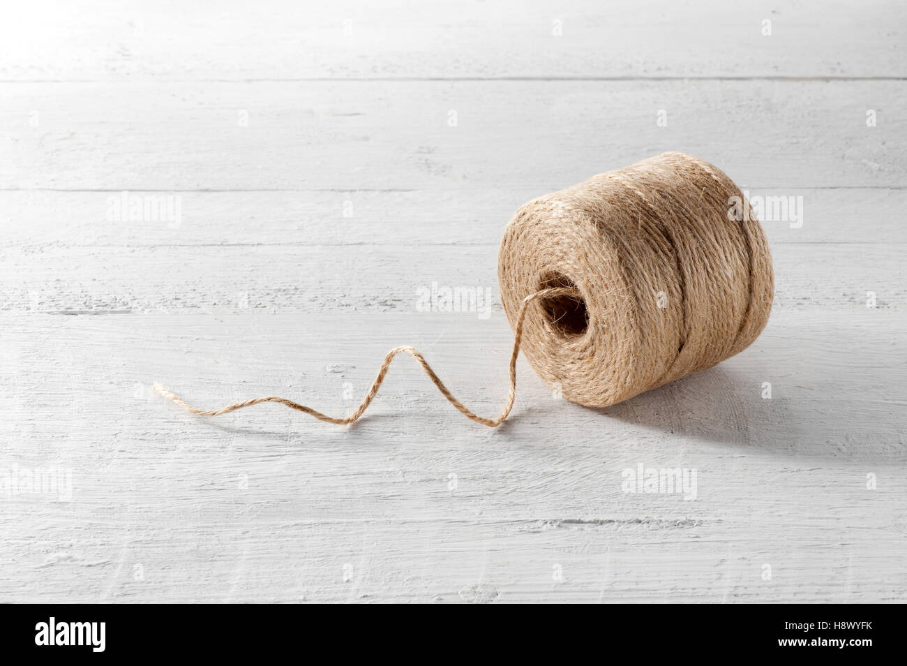 La bobine de ficelle brun grossier fabriqué à partir de fibres de chanvre naturel sur une planche de bois blanc avec un seul thread Banque D'Images