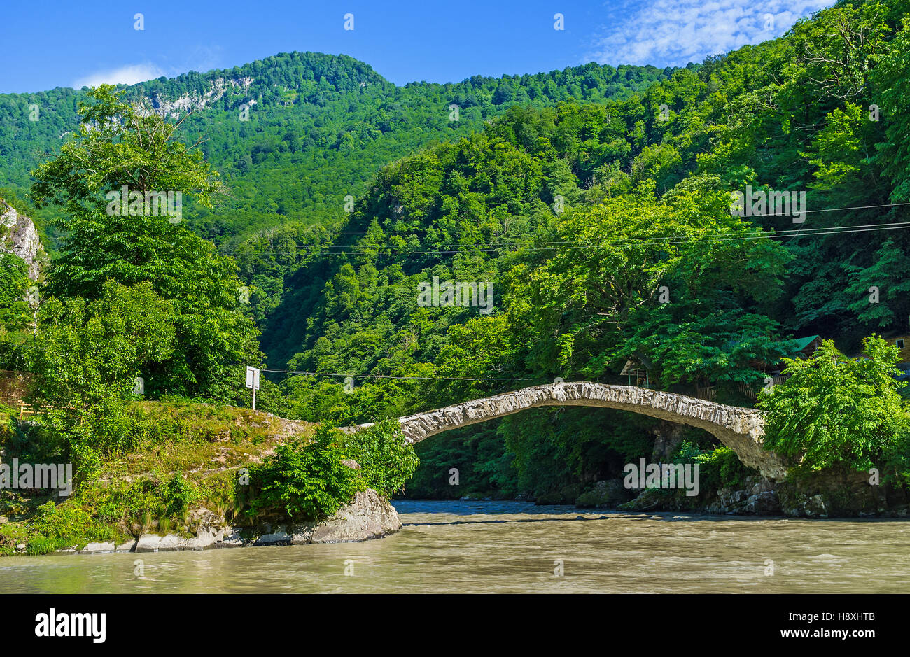 La pierre de la Reine Tamar voûté pont sur la rivière de montagne relie les rives verdoyantes de la vallée, Mahuntseti, Géorgie. Banque D'Images