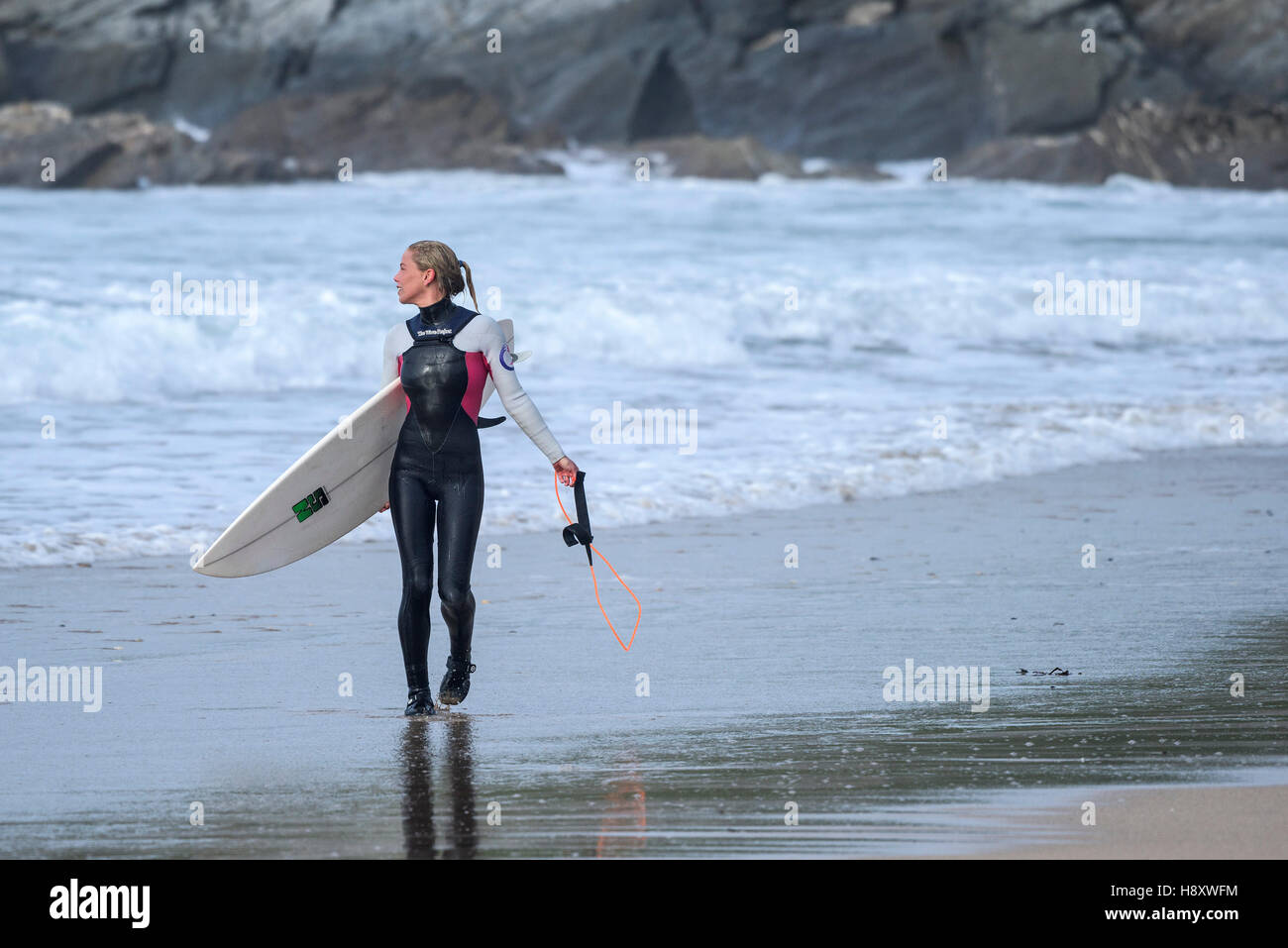 Un surfeur femelle promenades le long de la plage de Fistral à Newquay, Cornwall. Banque D'Images