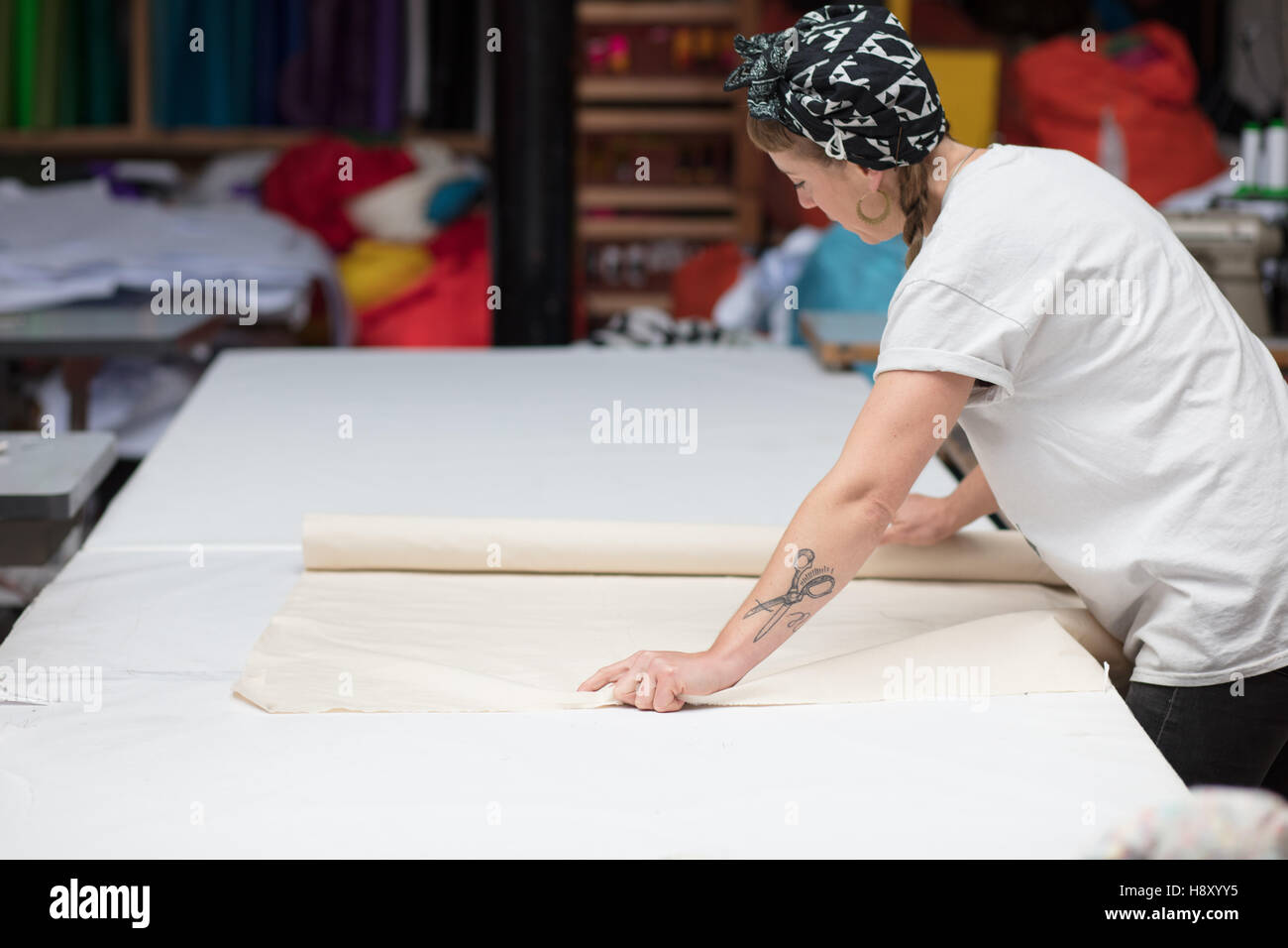 Jeune couturière tatouée le déploiement de tissu sur une table Banque D'Images