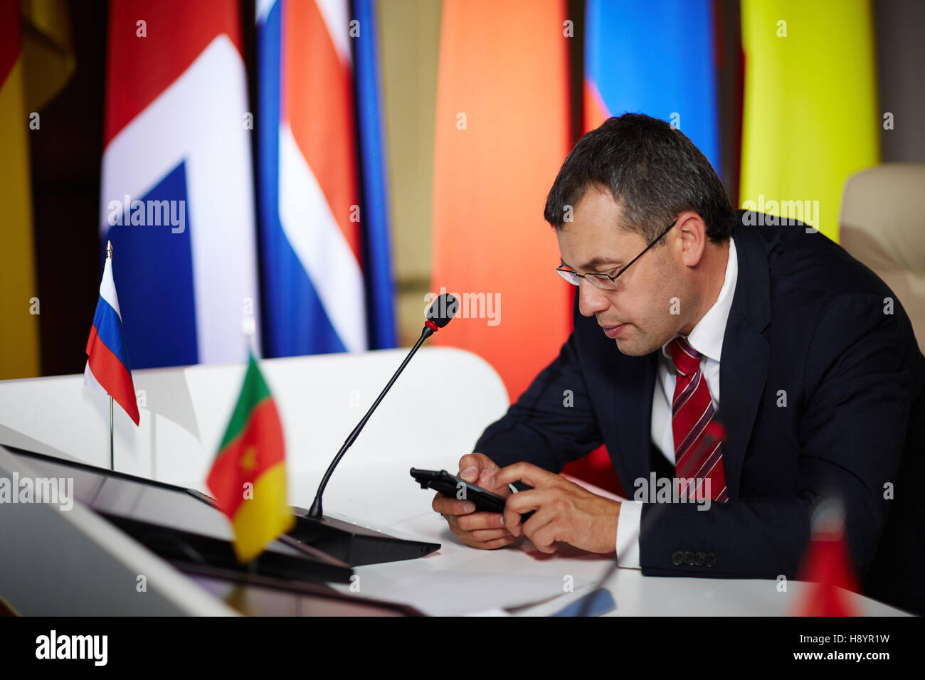 Homme politique moderne avec lecture des sms smartphone avec questions des spectateurs en tribune Banque D'Images