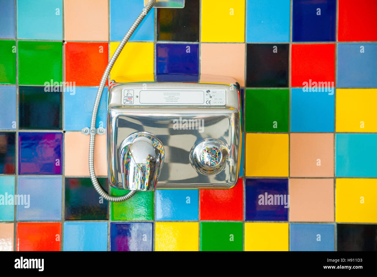 Un sèche-mains en métal monté sur un mur carrelé de couleur. Banque D'Images