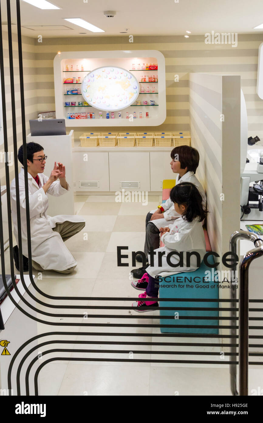 Le Japon, Nishinomiya, KidZania. Parc de jeux pour enfants. 2 enfants, garçon, fille, en blouse blanche de laboratoire blanc assis à l'écoute de conférences en Yakult lab. Banque D'Images