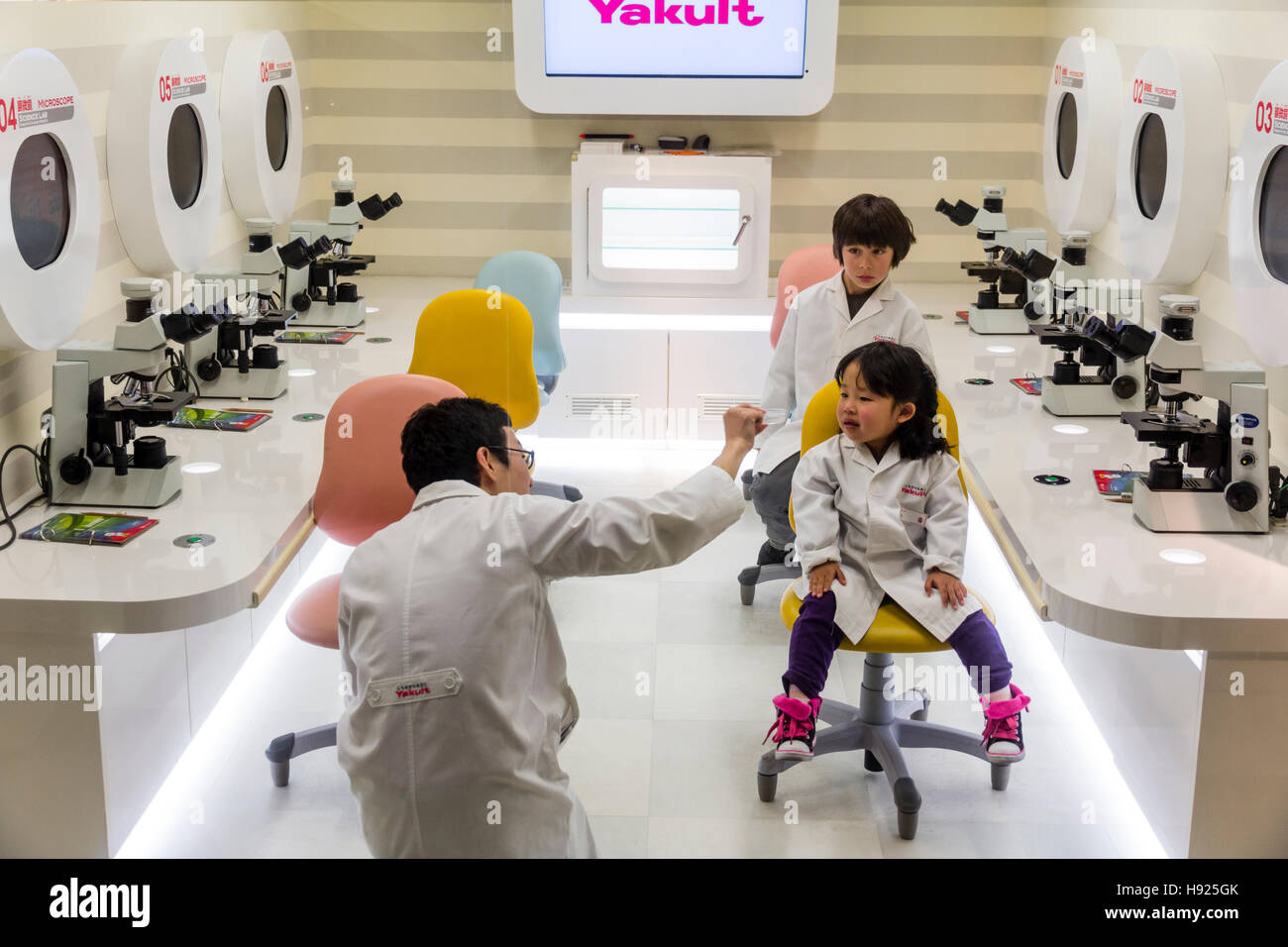 Le Japon, Nishinomiya, KidZania. Parc de jeux pour enfants. 2 enfants, garçon, fille, en blouse blanche de laboratoire blanc assis à l'écoute de conférences en Yakult lab. Banque D'Images