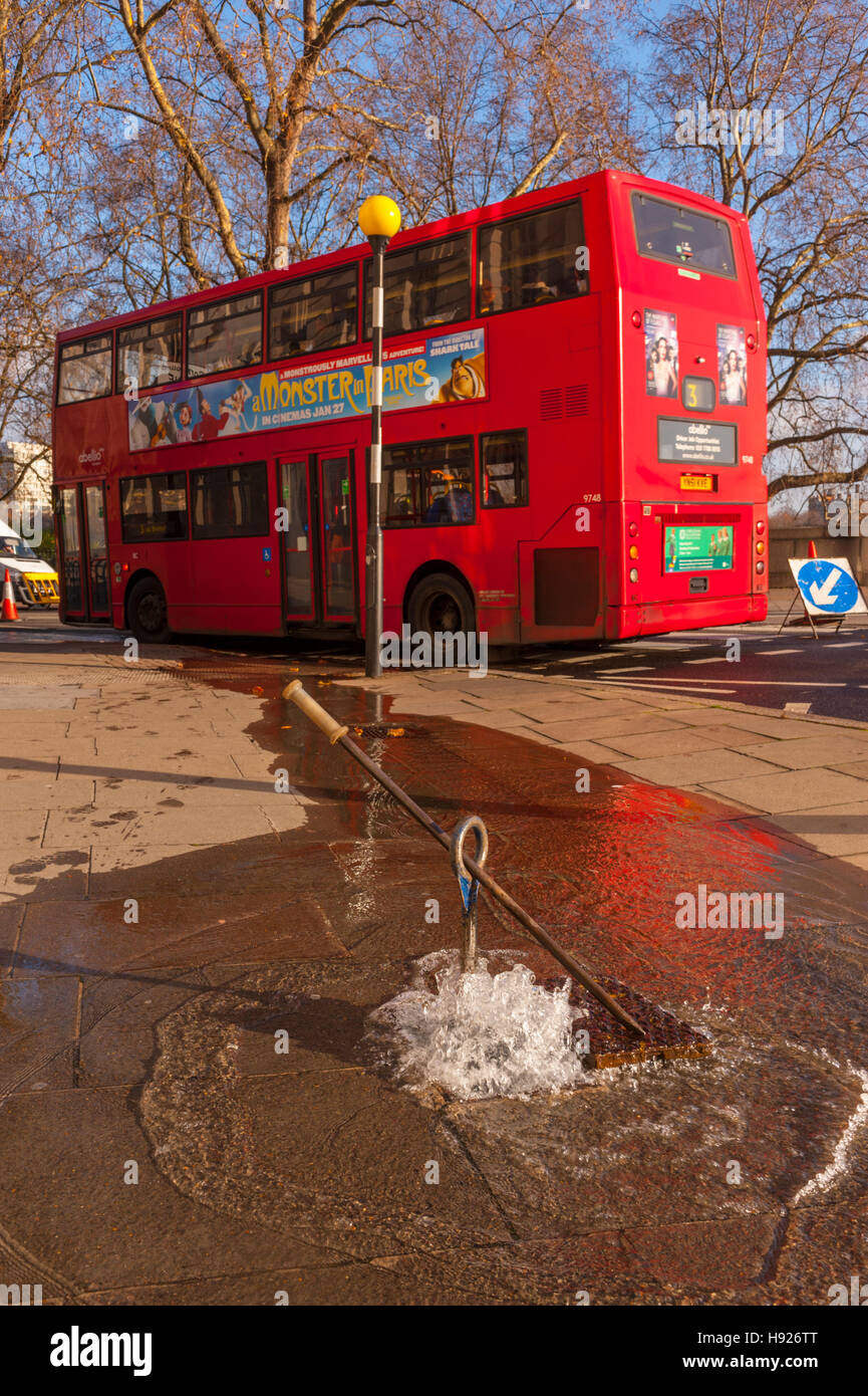 London bus rouge qui passent l'injection d'eau hors d'un trou d'une rafale d'eau principale Banque D'Images