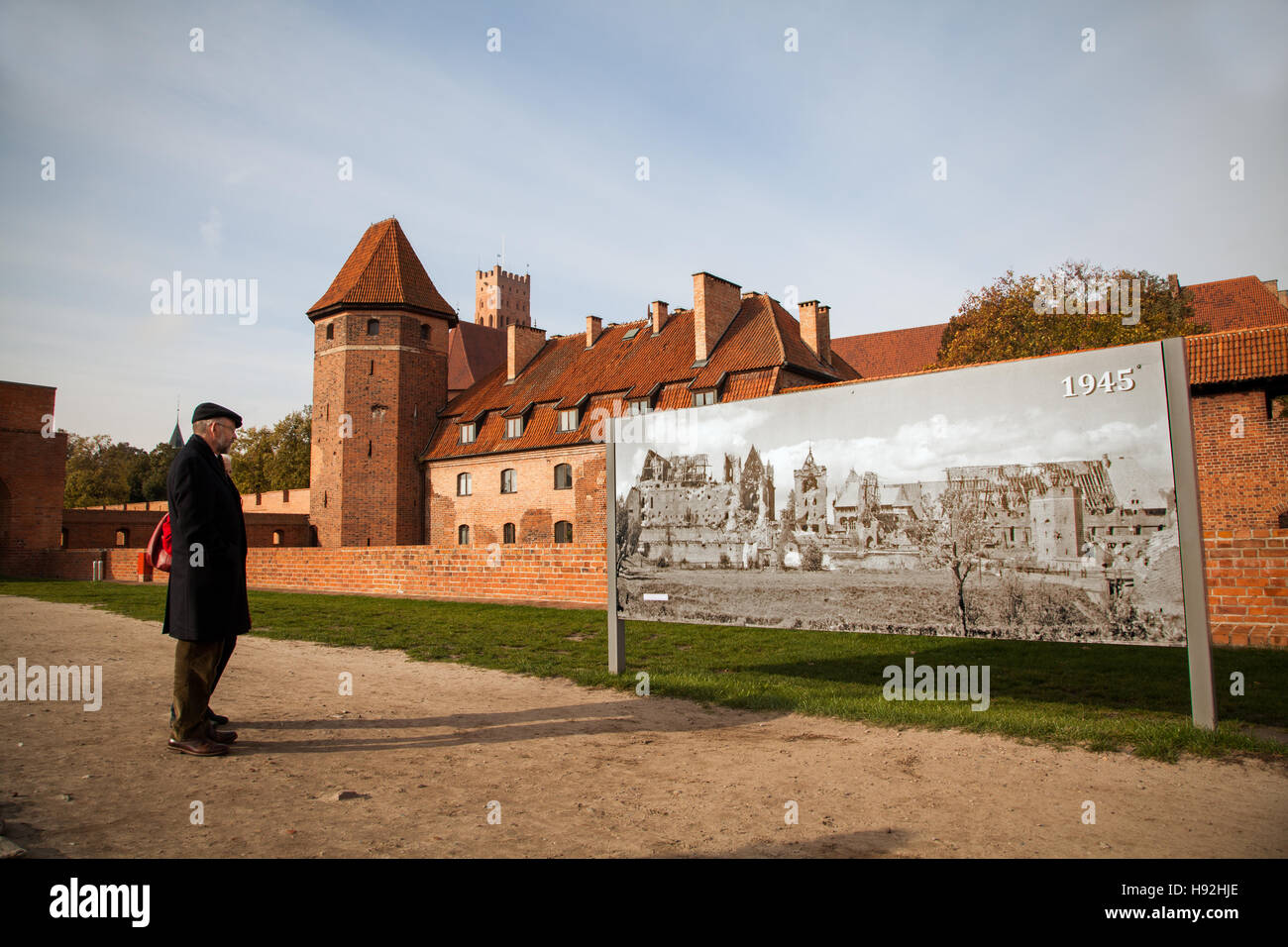 Homme debout à l'extérieur le château de Malbork Pologne regarder une affiche montrant les destructions causées pendant la seconde guerre mondiale Banque D'Images