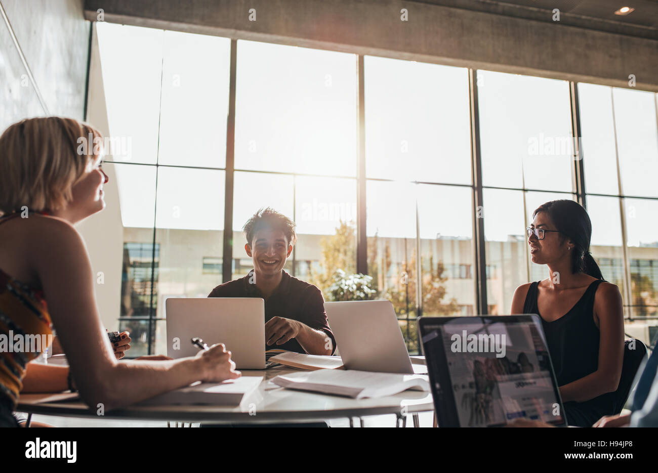 Jeunes étudiants assis autour d'une table dans une bibliothèque avec des livres et un ordinateur portable. étudiants universitaires qui étudient en groupe à la bibliothèque. Banque D'Images