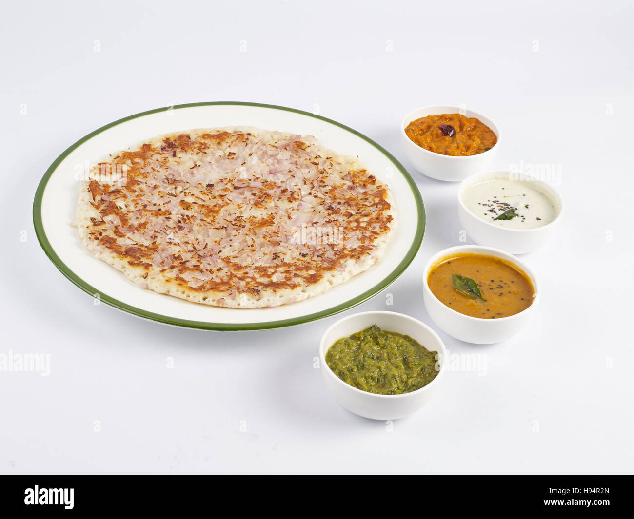 L'uthappam à l'oignon dans une assiette servie avec sambar et trois types de chutneys est un tiffin traditionnel de l'Inde du Sud sur fond blanc Banque D'Images