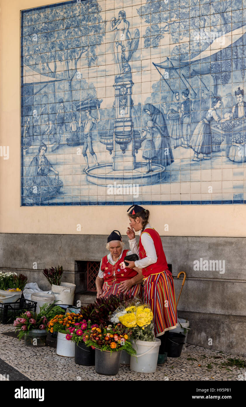 Les vendeurs de fleurs en costume traditionnel de Madère Funchal au marché avec des fleurs tropicales colorées en face du panneau de carrelage bleu Banque D'Images