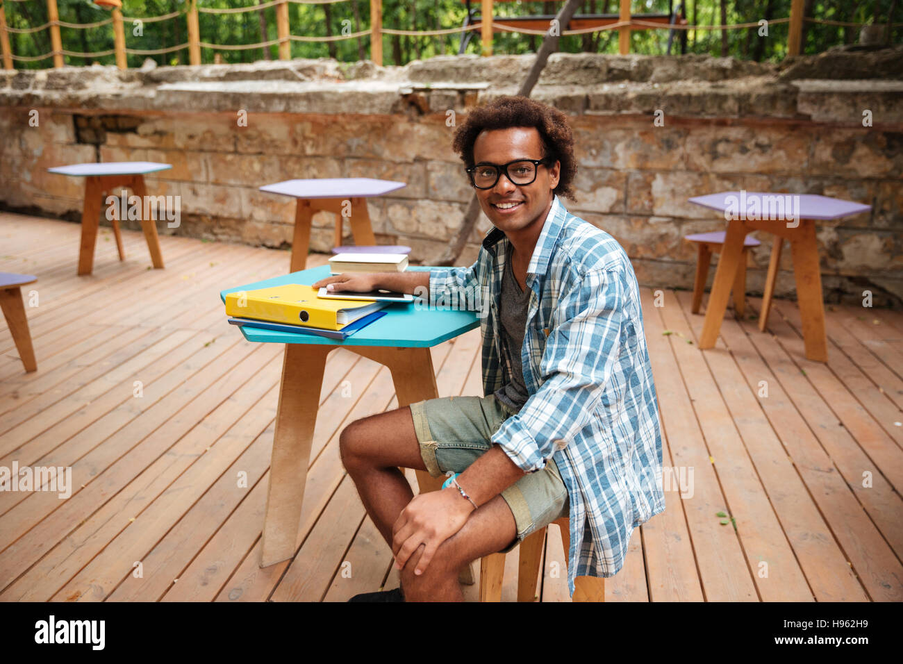 Cheerful young African man dans les verres et chemise à carreaux assis en terrasse d'un café Banque D'Images