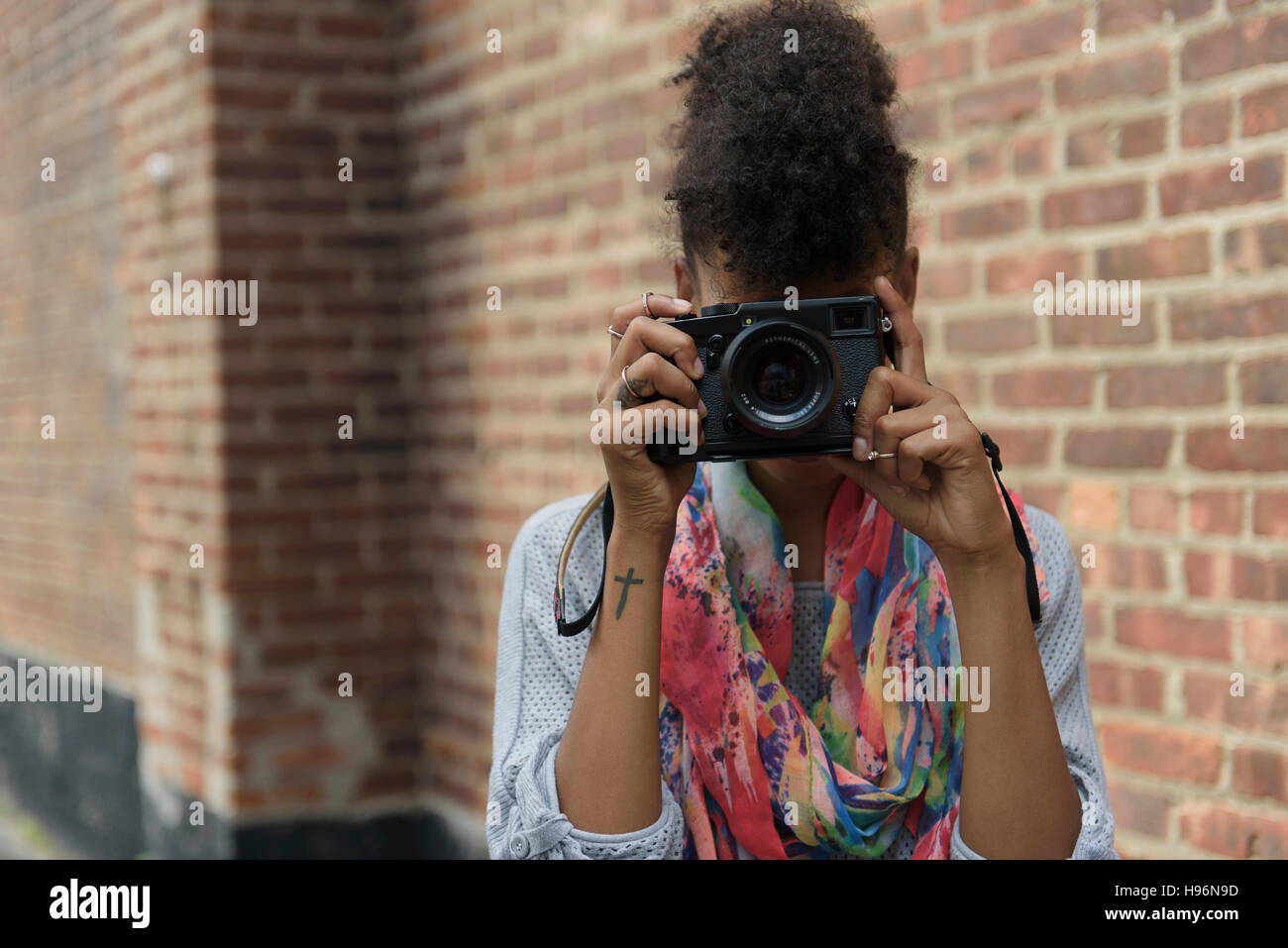 Young woman taking photo avec appareil photo numérique contre le mur de brique Banque D'Images