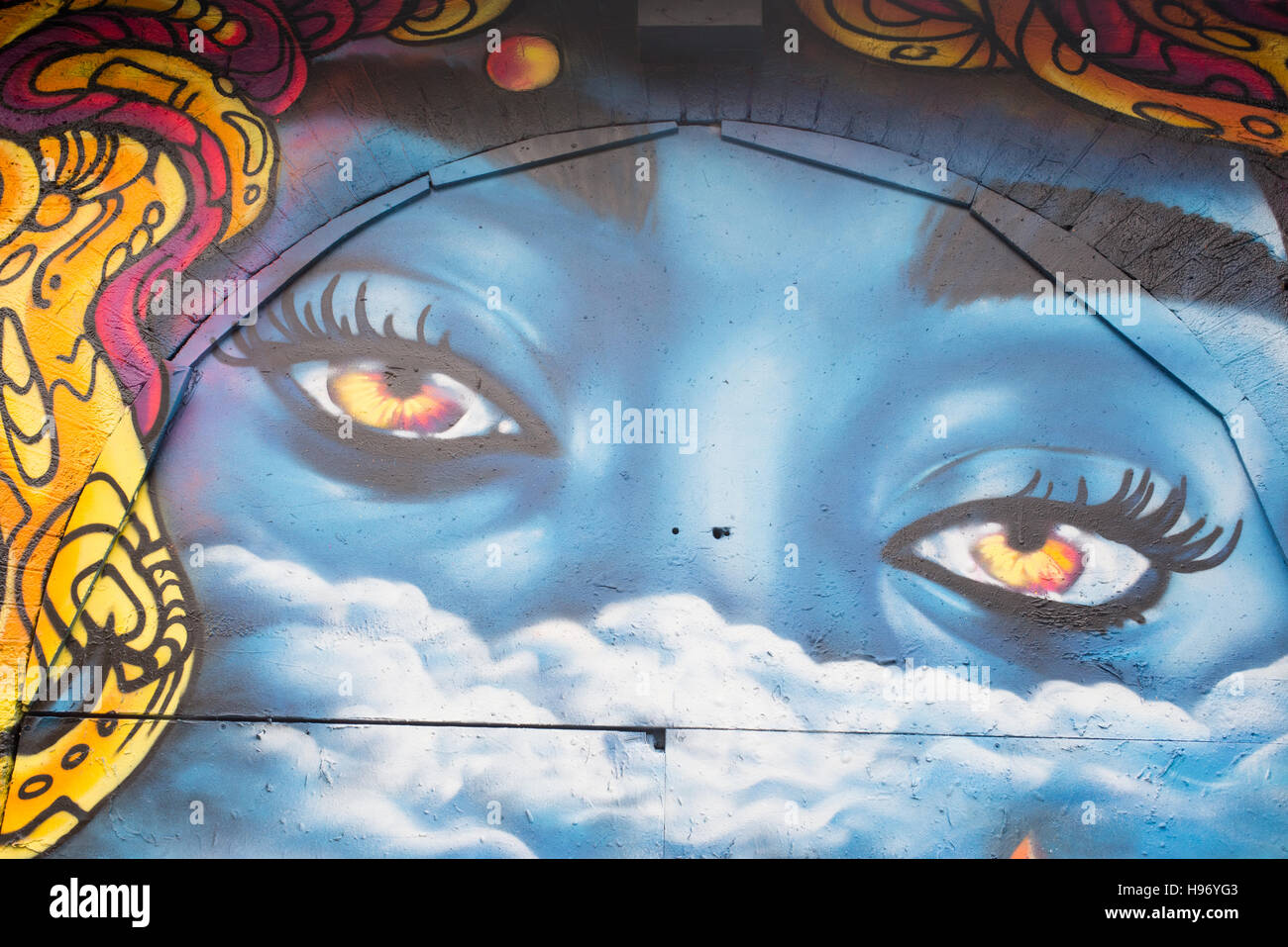 Graffiti sur mur avec face bleue et deux grands yeux ouverts, à regarder Banque D'Images