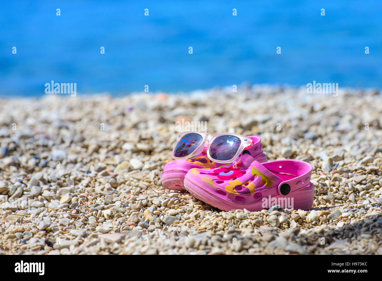 Plage rose kid's crocs et lunettes de soleil sur la plage de sable.sandales  de plage et lunettes de soleil dans le premier plan et la mer en  arrière-plan flou Photo Stock -