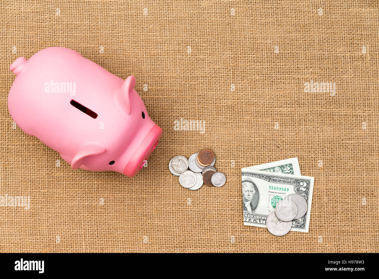 Pile de trésorerie USD dollar lâche avec billets et pièces alimentant une faim pink piggy bank dans un concept de l'épargne, la richesse et la planification de la retraite dans un d Banque D'Images