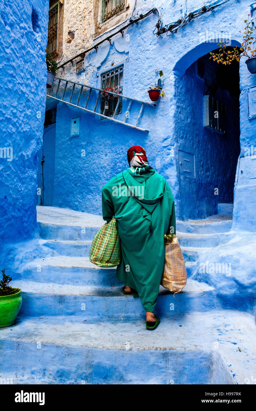 Une vieille femme marche dans les rues colorées de la Médina avec des sacs lourds, Chefchaouen, Maroc Banque D'Images