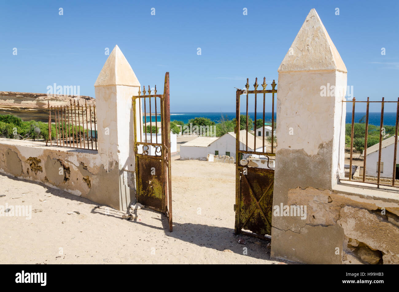 Metal Gate en ruine de mur en pierre donnant sur belle coloniale océan dans petit village de pêcheurs Mucuio en Angola. Banque D'Images