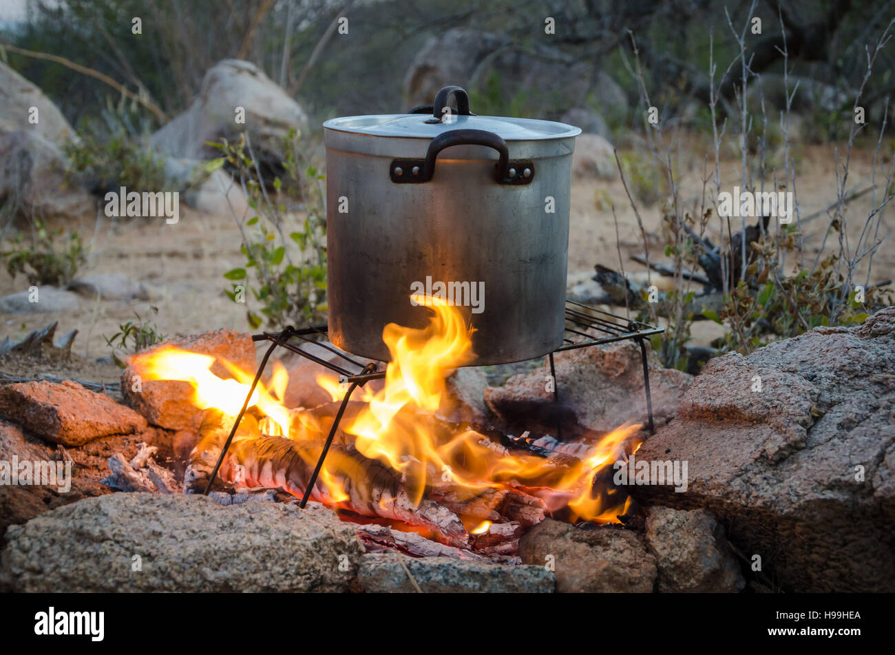 Casserole en aluminium pliable sur grill étant chauffé sur feu de camp en plein air entourée de rochers. Banque D'Images