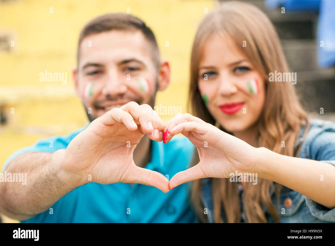 Jeune couple avec la peinture pour le visage formant coeur avec les mains Banque D'Images
