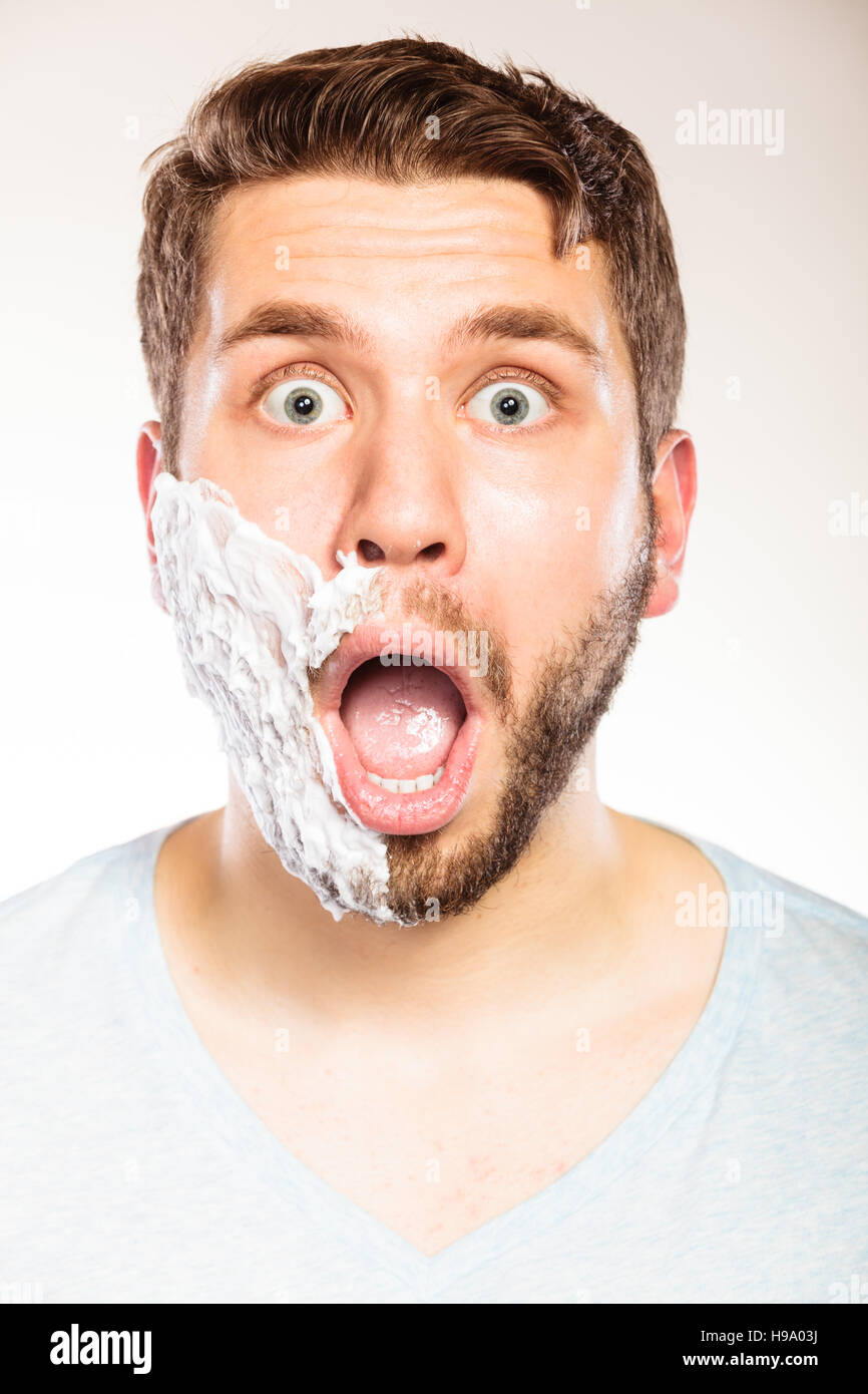 Jeune homme surpris choqué avec la crème à raser mousse sur la moitié du  visage barbe. Beau gars de la préparation pour le rasage. Hygiène et soins  de la peau Photo Stock -