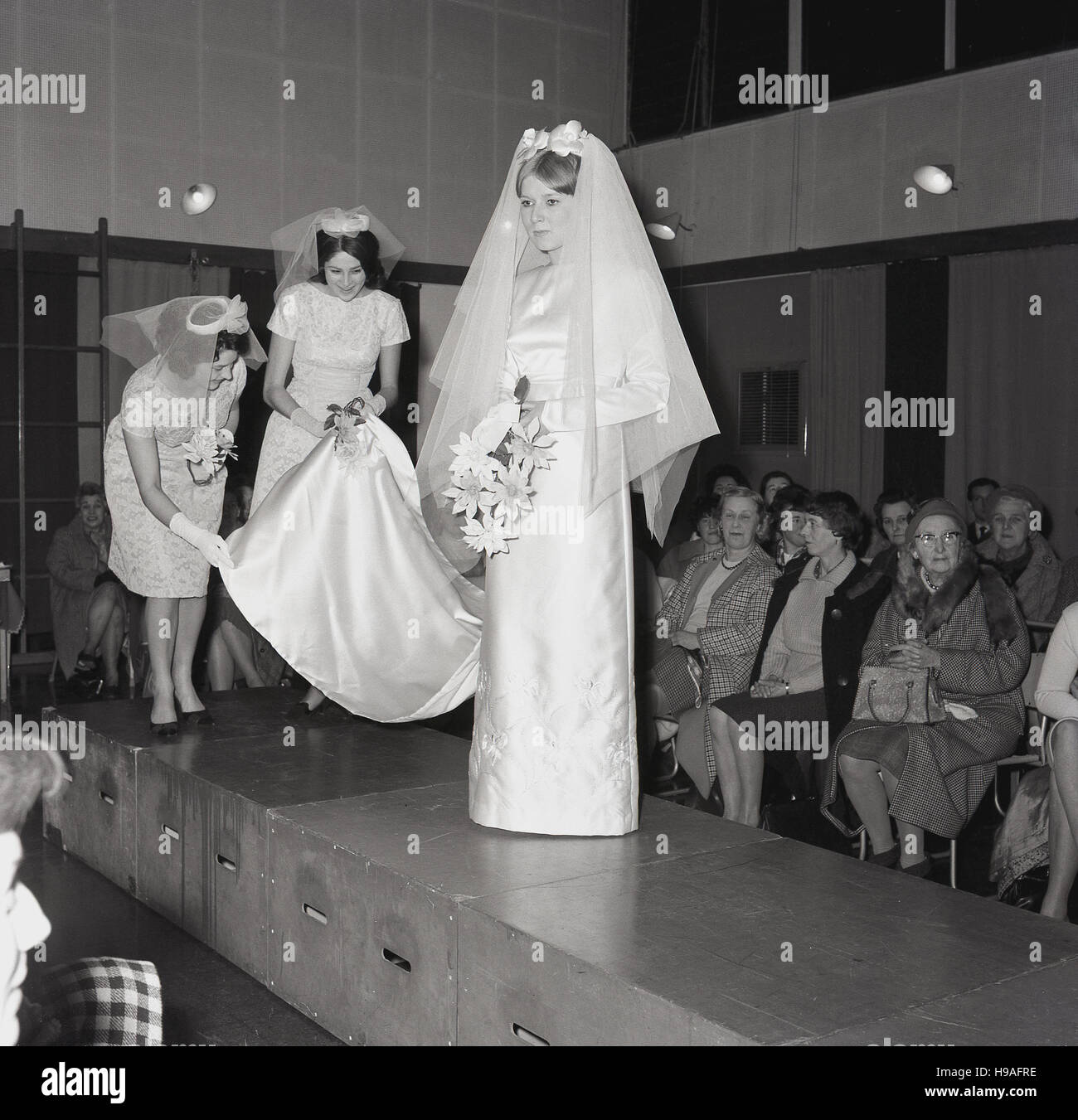 1965, historiques, Grande-Bretagne, Suite Nuptiale, Salon modèle féminin avec l'appui portant le long de la cathédrale, promenades le long d'une plate-forme surélevée pour démontrer le dernier modèle dans des robes ou des robes à un public assis. Banque D'Images