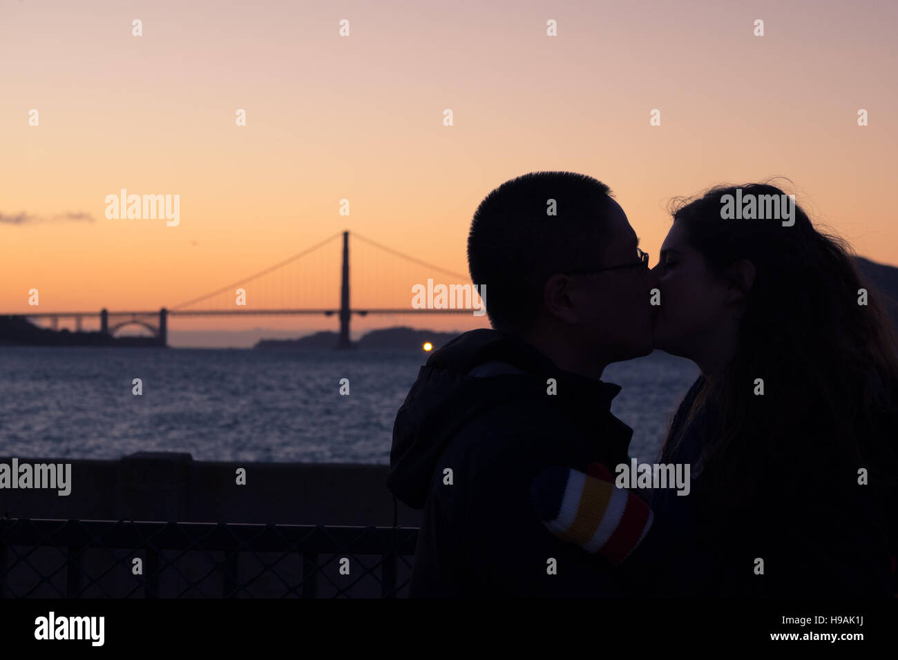 Un jeune couple baiser au coucher du soleil en face du Golden Gate Bridge à San Francisco, Californie. Banque D'Images