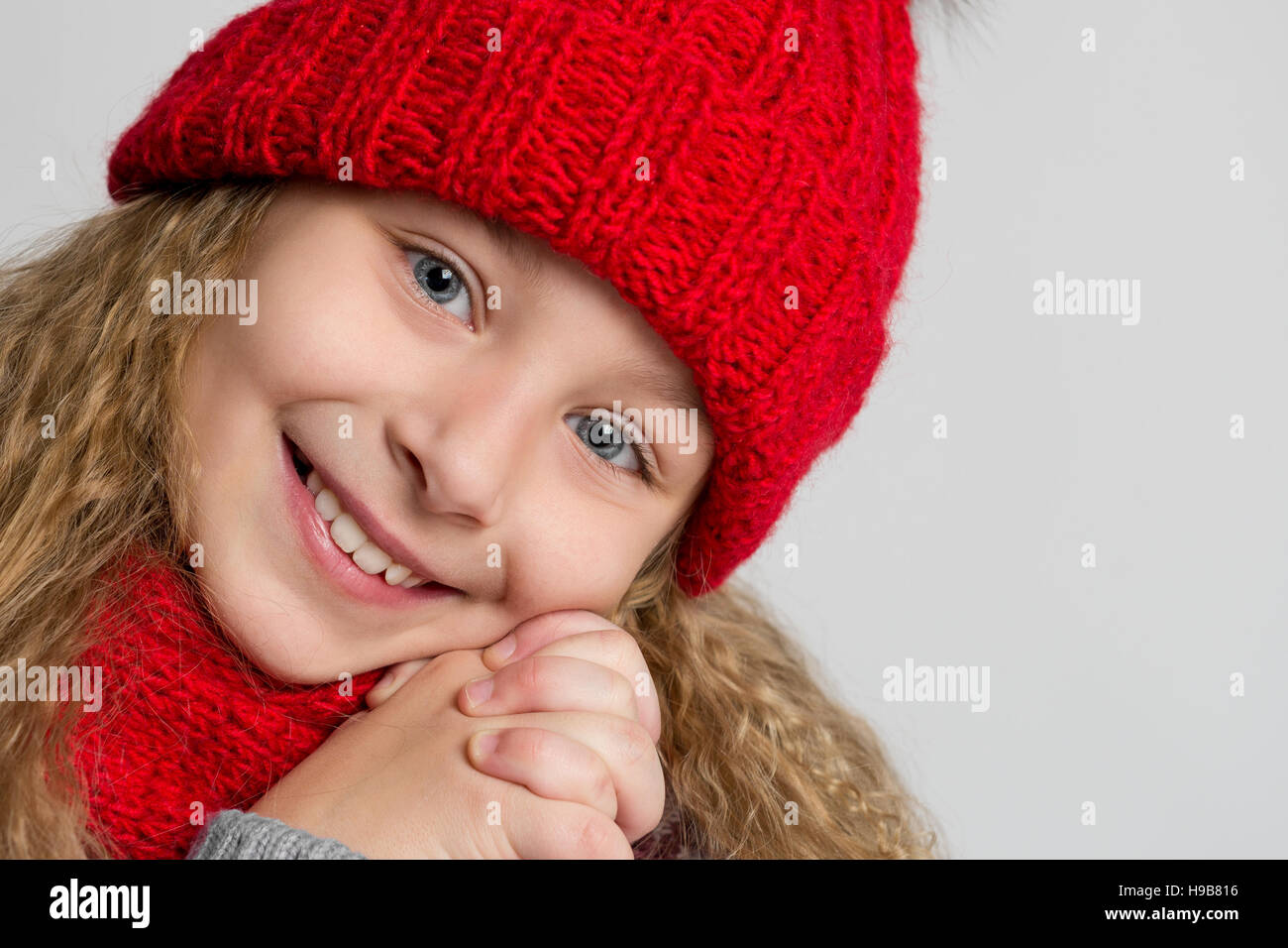 Portrait d'une belle petite fille au chapeau tricoté rouge sur un fond gris. Visage d'un enfant heureux libre Banque D'Images