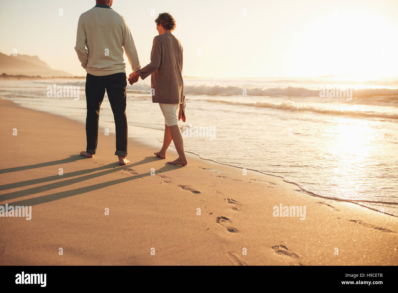 Vue arrière d'un couple en train de marcher le long du bord de mer. L'homme et la femme mature ensemble nous promener sur le bord de la mer au coucher du soleil. Banque D'Images