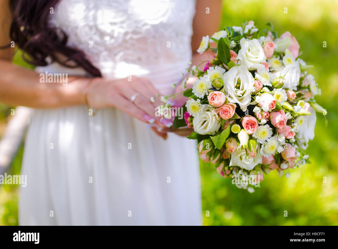 Bride holding a bouquet de mariage avec des roses sur fond vert au cours de l'été Banque D'Images