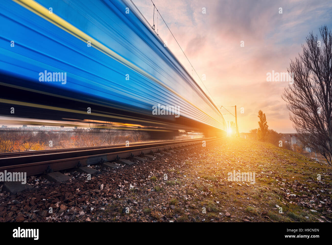 Bleu haute vitesse train de voyageurs le railroad track in motion au coucher du soleil. Train de banlieue brouillée. La gare ferroviaire. Railroad travel Banque D'Images