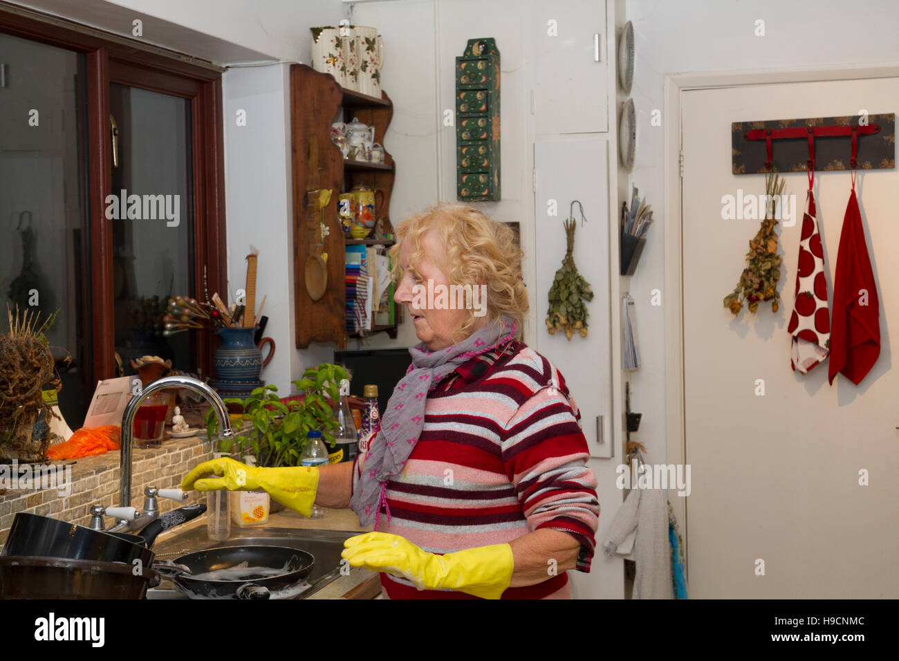 Debout à l'évier laver à la main, femme portant des gants en caoutchouc faisant la vaisselle, laver les tâches. Banque D'Images