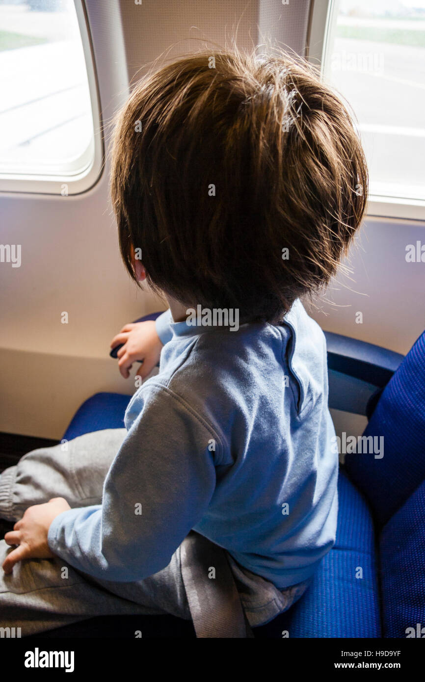 Caucasien enfant, garçon, 4-6 ans, assis dans le siège de l'avion en regardant par la fenêtre. Visage détourné. Banque D'Images