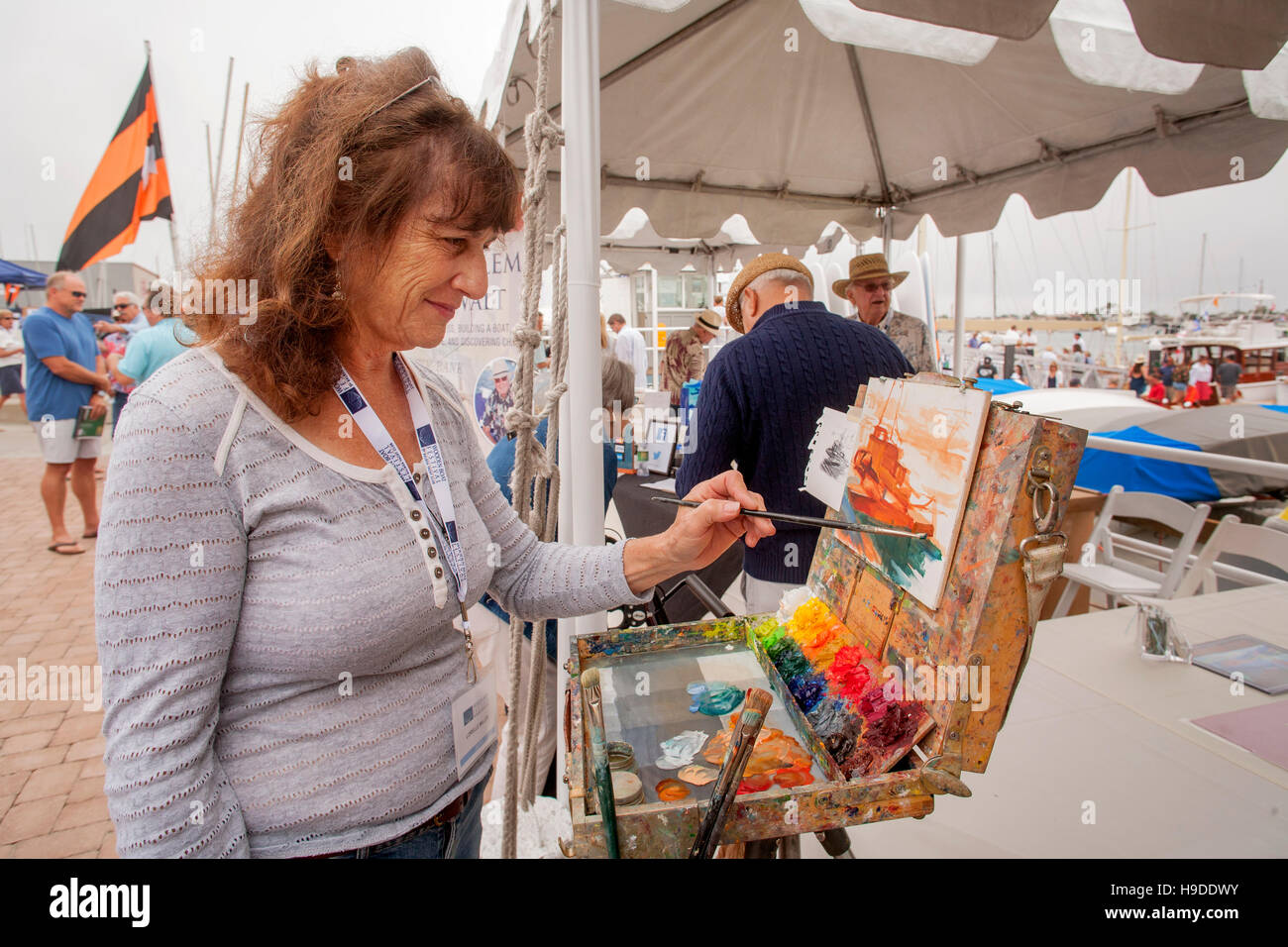 Une femme de race blanche artiste marin travaille à son chevalet dans un Newport Beach, CA, yacht club yacht yard représentant un navire dans le port. Remarque Les peintures colorées. Banque D'Images