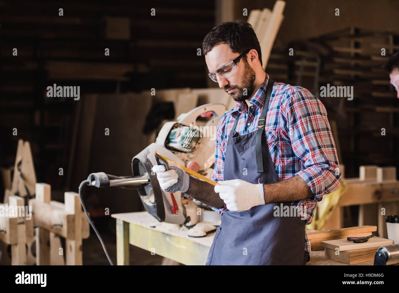 Beau Carpenter dans des lunettes, debout près de son objet en bois dans l'atelier Banque D'Images