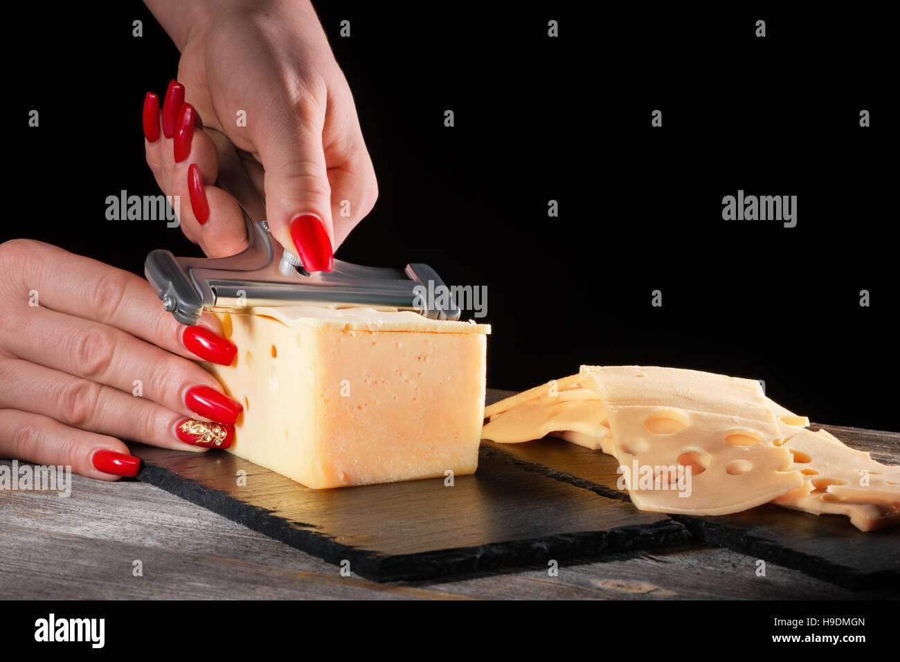 Femme avec de belles mains manucure lumineux whetstone couper le fromage à l'aide d'une plaque en ardoise noire sur slicer Banque D'Images