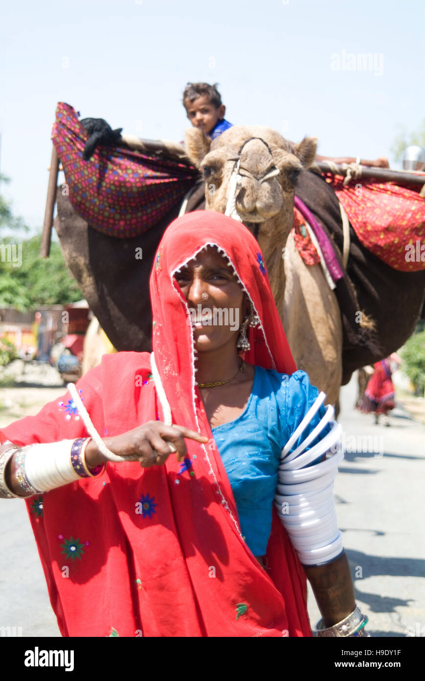 Une femme nomade mène son chameau rempli de biens matériels, y compris l'enfant, le long d'une route dans le sud du Rajasthan, Inde. Banque D'Images