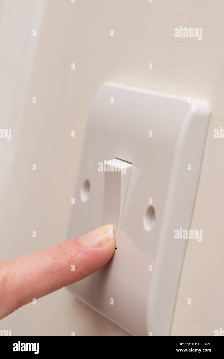 Close up. Un doigt appuie sur un seul interrupteur de lumière blanche sur un mur à la crème. COPY SPACE Banque D'Images