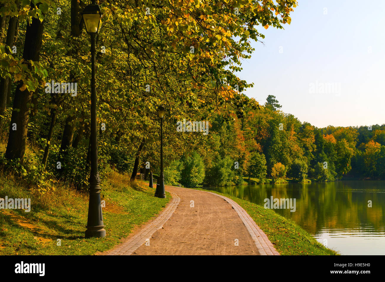 Autumn park paysage avec un chemin le long d'un étang et arbres éclairés par la lumière du soleil chaude. Banque D'Images