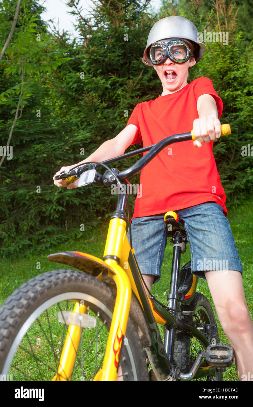 Cute teen boy wearing metal chaudron comme un casque et lunettes posant sur un vélo dans un parc d'été - un drôle de cycliste power concept Banque D'Images