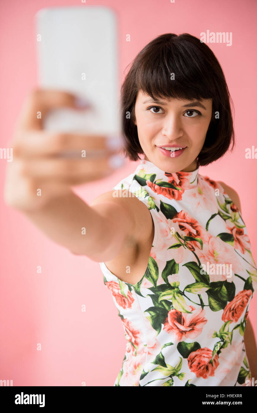Hispanic woman wearing dress posing floral pour selfies téléphone cellulaire Banque D'Images