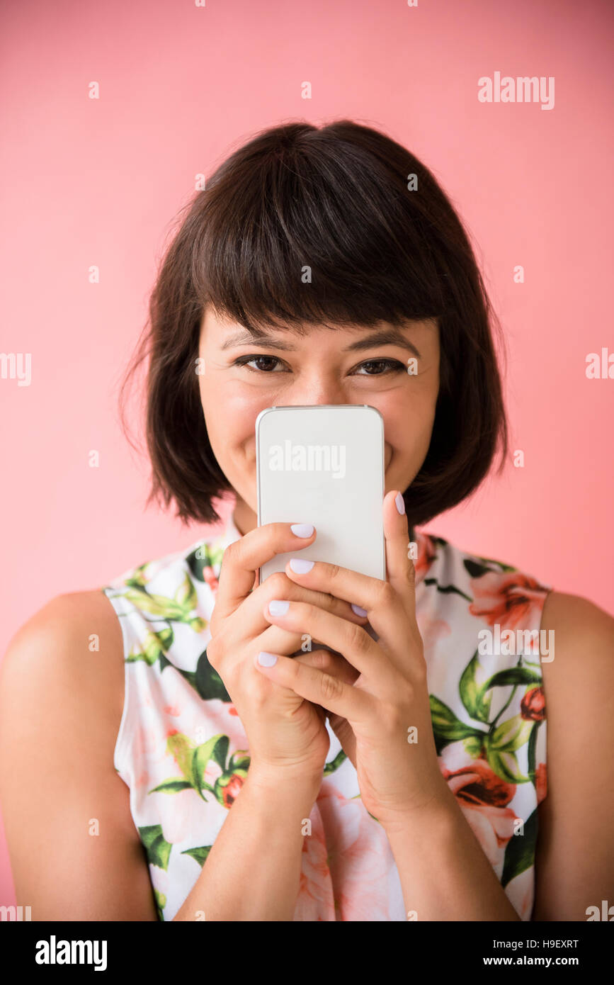 Femme hispanique se cachant derrière cell phone Banque D'Images