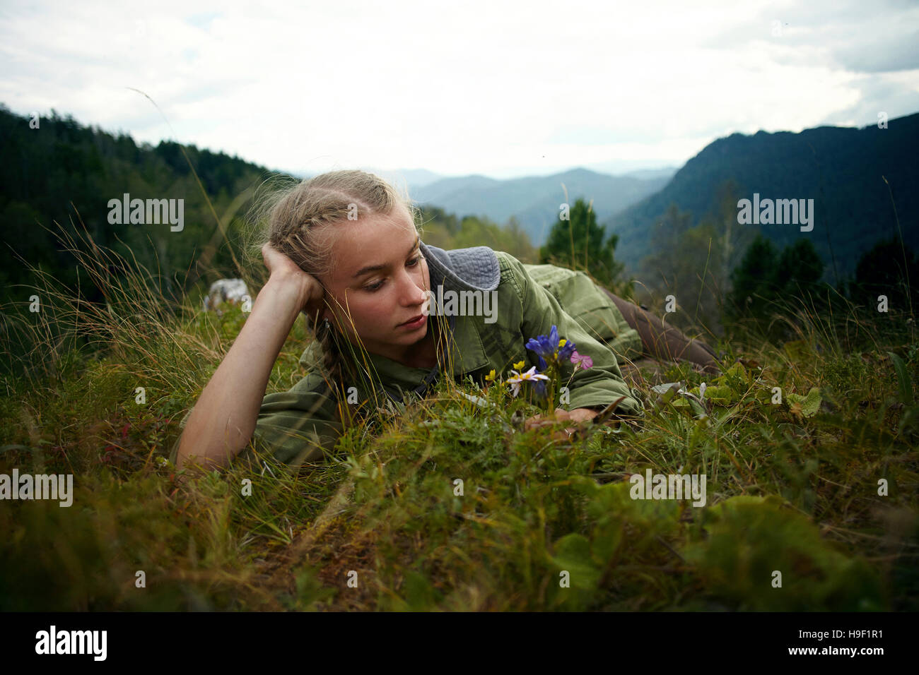Caucasian girl holding wildflowers laying in grass sur hill Banque D'Images